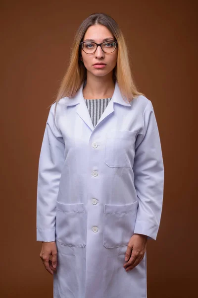 Portrait of young beautiful woman doctor against brown background — Stock Photo, Image