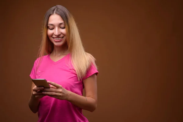 Happy young beautiful woman using mobile phone against brown background — Stock Photo, Image