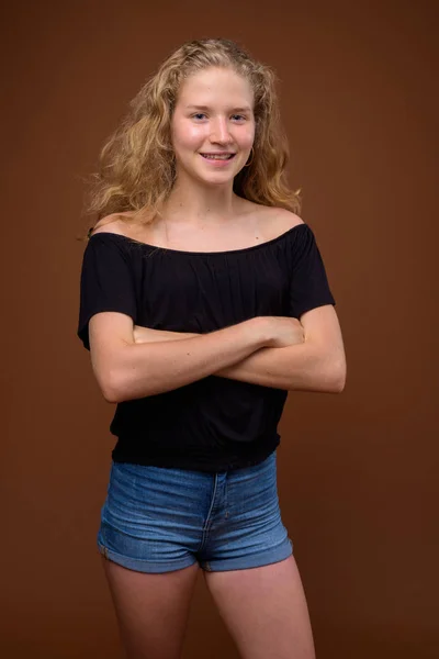Mooie blonde tiener meisje glimlachend tegen bruine achtergrond — Stockfoto