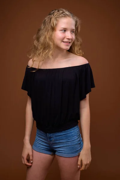 Unga vackra blonda tonårstjej som ler mot brun bakgrund — Stockfoto