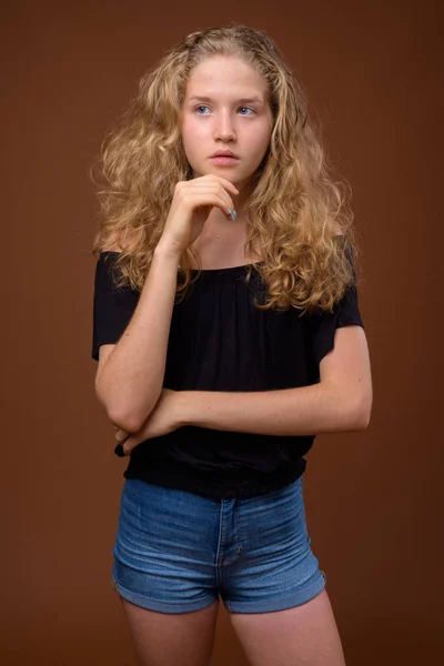 年轻美丽的金发少女思考在棕色背景 — 图库照片