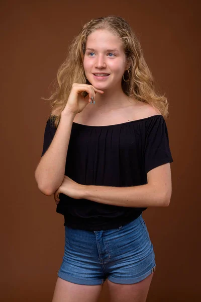 Young beautiful blonde teenage girl thinking against brown background — Stock Photo, Image