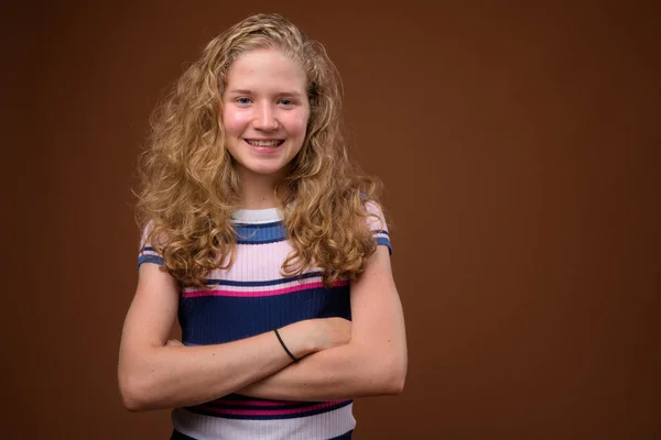 Mooie blonde tiener meisje glimlachend tegen bruine achtergrond — Stockfoto