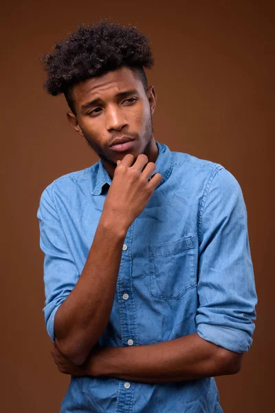 Young serious African man thinking against brown background — Stock Photo, Image