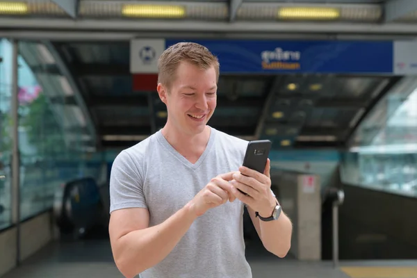 Young happy tourist man using phone in front the train station in Bangkok — Stock Photo, Image