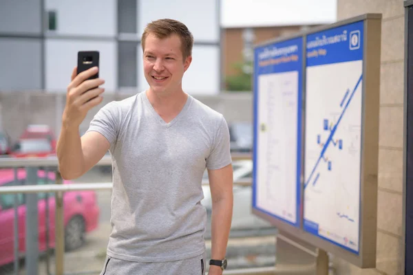 Νέοι ευτυχισμένη τουριστικά άνθρωπος λαμβάνοντας αυτοπορτρέτα κατά την προβολή του χάρτη στο σταθμό του τρένου στην Μπανγκόκ — Φωτογραφία Αρχείου
