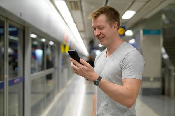 Νέοι ευτυχισμένη τουριστικά άνθρωπος χρησιμοποιώντας το τηλέφωνο στο σταθμό του μετρό στην Μπανγκόκ — Φωτογραφία Αρχείου