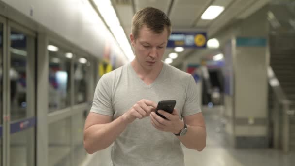 Молодой счастливый турист пользуется телефоном на станции метро в Бангкоке — стоковое видео