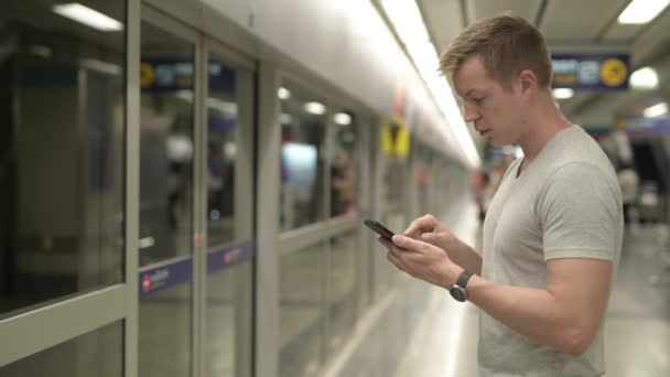 Вид профілю молодих туристичних людини за допомогою телефону в очікуванні поїзда в Бангкоку — стокове відео