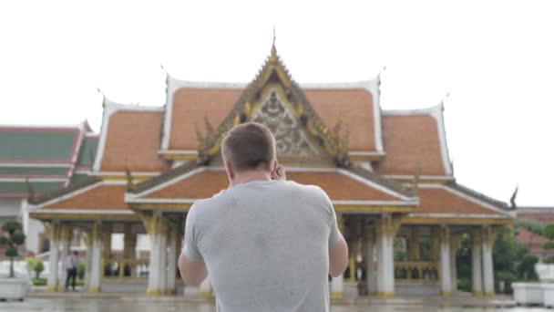 バンコクの仏教寺院のビューに対して若いハンサムな観光客の男のポートレート — ストック動画