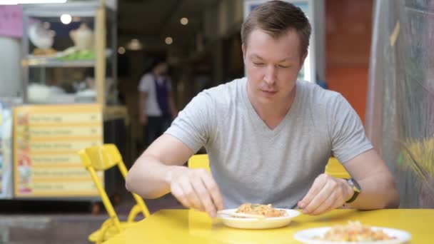 Jonge gelukkig toeristische man eten Pad Thaise noedels in Bangkok Khaosan Road — Stockvideo