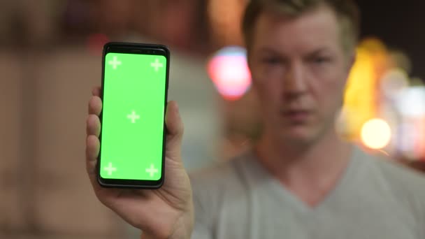 Visage de jeune touriste heureux montrant téléphone avec écran vert à Chinatown la nuit — Video