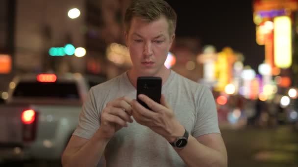 Jovem turista feliz usando telefone contra vista das ruas em Chinatown à noite — Vídeo de Stock