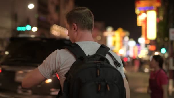 Vista trasera del joven turista mochilero usando el teléfono en Chinatown por la noche — Vídeo de stock