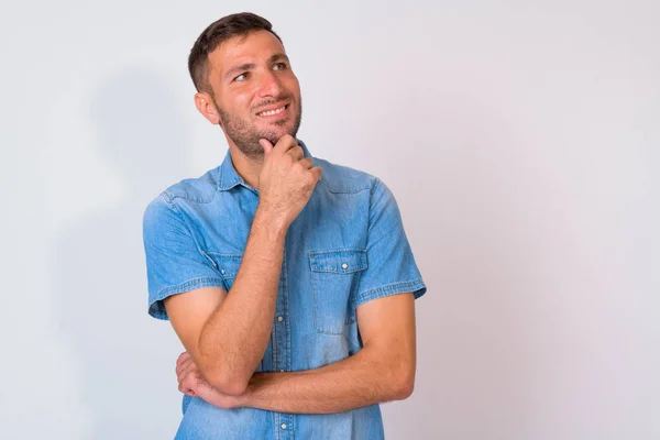 Glücklicher bärtiger persischer Mann denkt, während er vor weißem Hintergrund aufblickt — Stockfoto