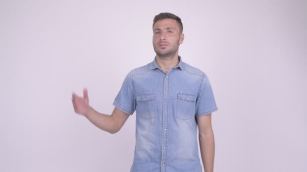 Feliz hombre persa barbudo sonriendo mientras muestra algo sobre fondo blanco — Vídeos de Stock