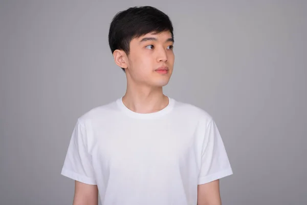 Studio shot of young Asian man thinking while looking away — Stock Photo, Image
