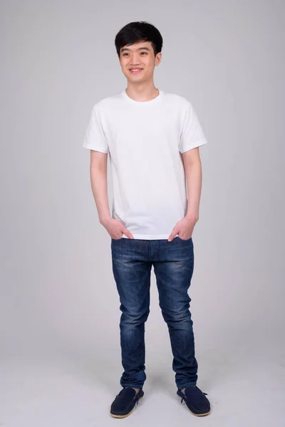 Ganzkörperaufnahme junger glücklicher asiatischer Mann im Stehen und Denken — Stockfoto