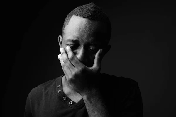 Studio shot of young African man wearing black shirt against black background in black and white