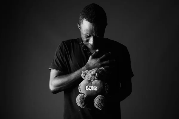Sad young African man with teddy bear and love sign text in black and white
