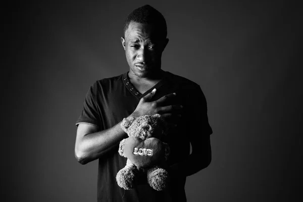 Sad young African man with teddy bear and love sign text in black and white — Stock Photo, Image