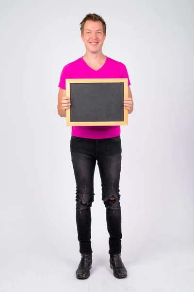 Ganzkörperaufnahme eines glücklichen jungen gutaussehenden Mannes, der lächelt, während er eine Tafel hält — Stockfoto