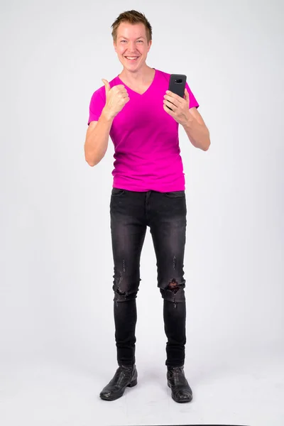 Полный снимок счастливого молодого человека, использующего телефон и показывающего большие пальцы — стоковое фото