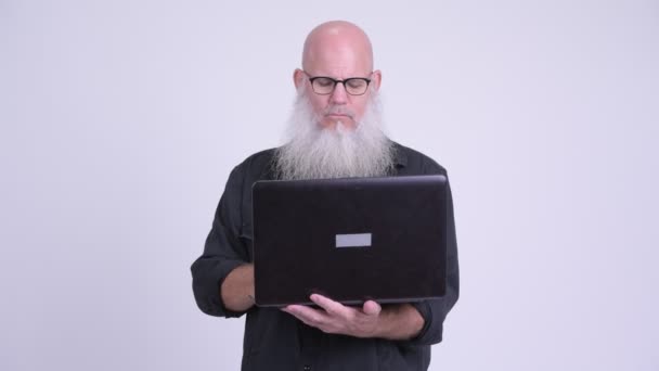Зрелый лысый бородатый мужчина думает во время использования ноутбука — стоковое видео