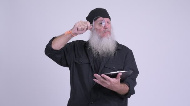 Ώριμη γενειοφόρος hipster άνθρωπος που κρατά το Πρόχειρο κατά τη χρήση του μεγεθυντικού φακού — Αρχείο Βίντεο