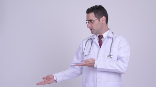 Bonito homem médico mostrando algo contra fundo branco — Vídeo de Stock