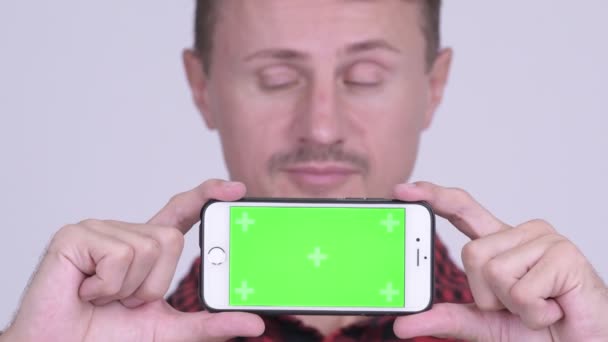 Cara de hombre hipster barbudo feliz pensando mientras muestra el teléfono — Vídeo de stock