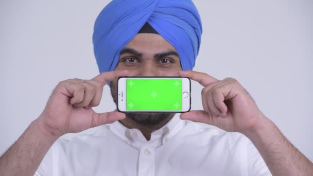 Față de fericit tânăr barbă indian Sikh om gândire în timp ce arată telefon — Videoclip de stoc