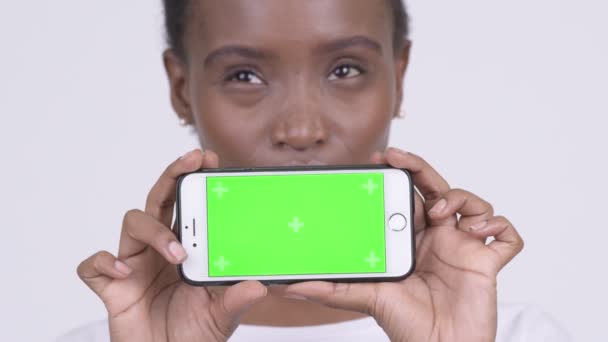 Gesicht einer glücklichen jungen schönen Afrikanerin, die beim Vorzeigen ihres Telefons denkt — Stockvideo