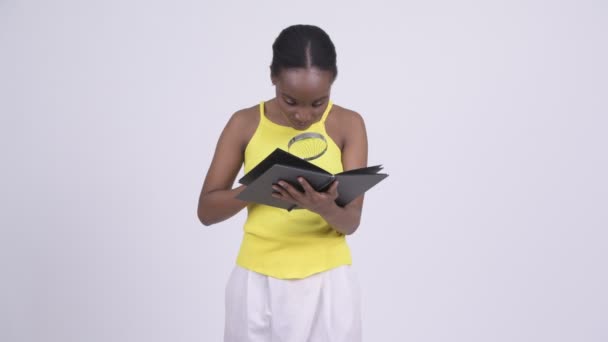 Молодая красивая африканская женщина читает книгу с лупой — стоковое видео