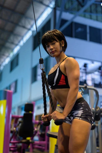 Jovem mulher no ginásio fazendo tricep pushdown com corda — Fotografia de Stock