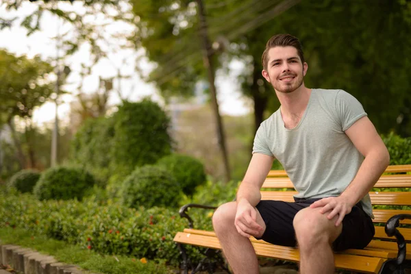 Portret van de jonge knappe man zit in het park tijdens het glimlachen — Stockfoto