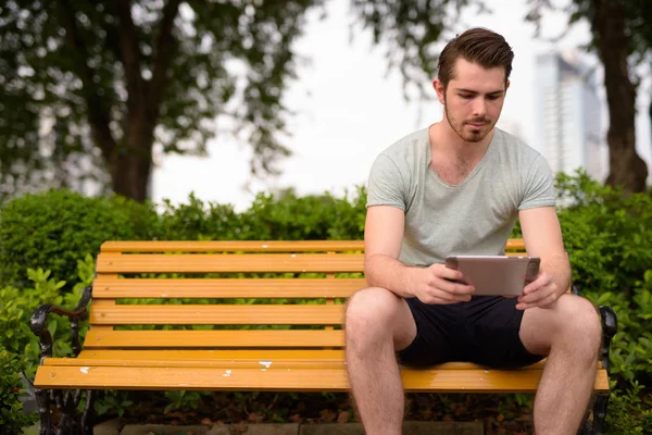 Ung man sitter vid park medan använder digitala tablett dator — Stockfoto