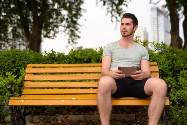 Ung man sittande på park använder digitala tablett och tänkande — Stockfoto