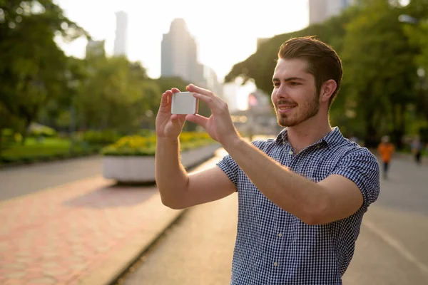 Man relaxing at the park while taking picture using mobile phone — Stock Photo, Image