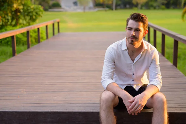 Portret van de jonge knappe man zitten en denken in het park — Stockfoto