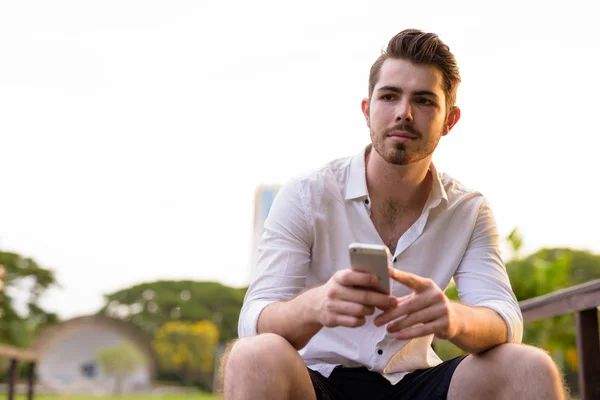 Homme assis et utilisant le téléphone mobile dans le parc tout en pensant — Photo