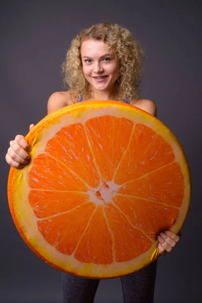 Young beautiful woman holding big slice of orange fruit — Stock Photo, Image