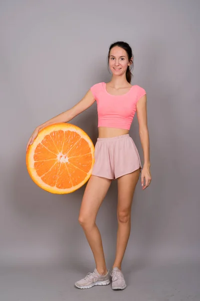 Jovem mulher bonita pronta para ginásio segurando grande fatia de fruta laranja — Fotografia de Stock