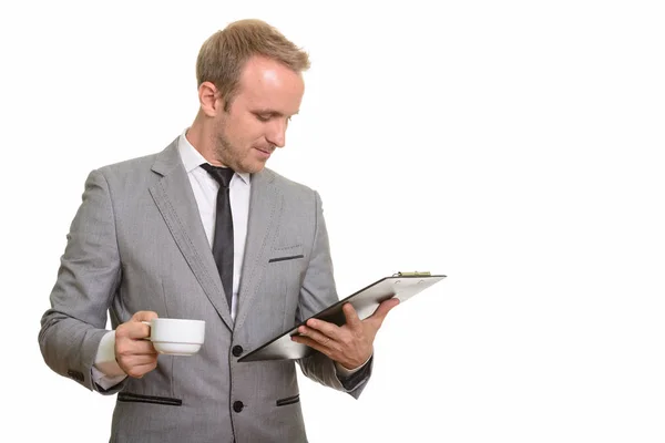 Handsome Caucasian businessman reading clipboard while drinking — Stock Photo, Image