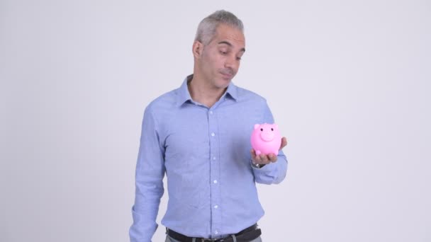 Glücklicher persischer Geschäftsmann mit Sparschwein gibt vor weißem Hintergrund die Daumen hoch — Stockvideo