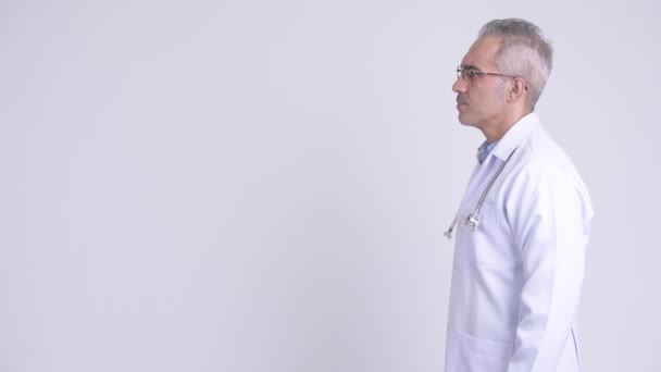 Profilansicht eines glücklichen persischen Mannes Arzt, der vor weißem Hintergrund denkt — Stockvideo