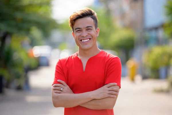 Feliz joven asiático hombre sonriendo con los brazos cruzados al aire libre —  Fotos de Stock