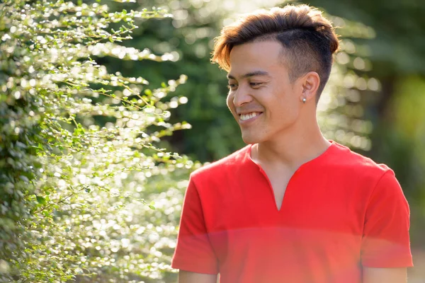 Feliz joven asiático hombre sonriendo y pensando con la naturaleza al aire libre —  Fotos de Stock