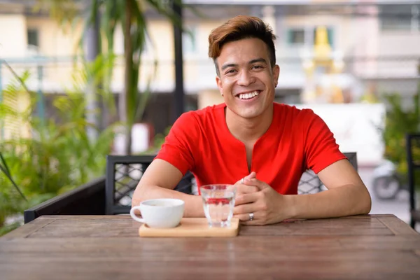 Feliz joven asiático hombre sonriendo en la cafetería al aire libre —  Fotos de Stock