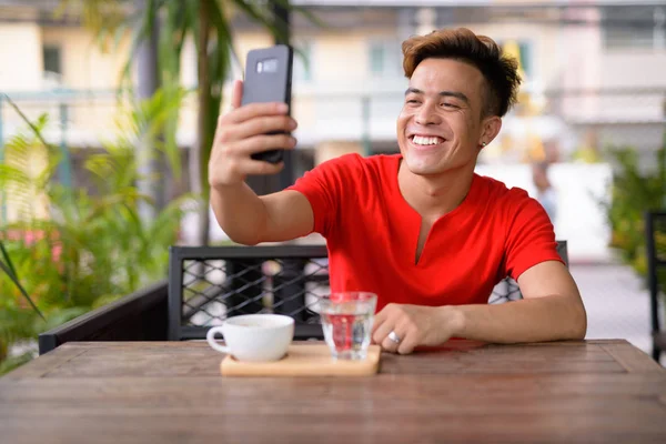 Счастливый молодой азиат делает селфи в кафе на открытом воздухе — стоковое фото